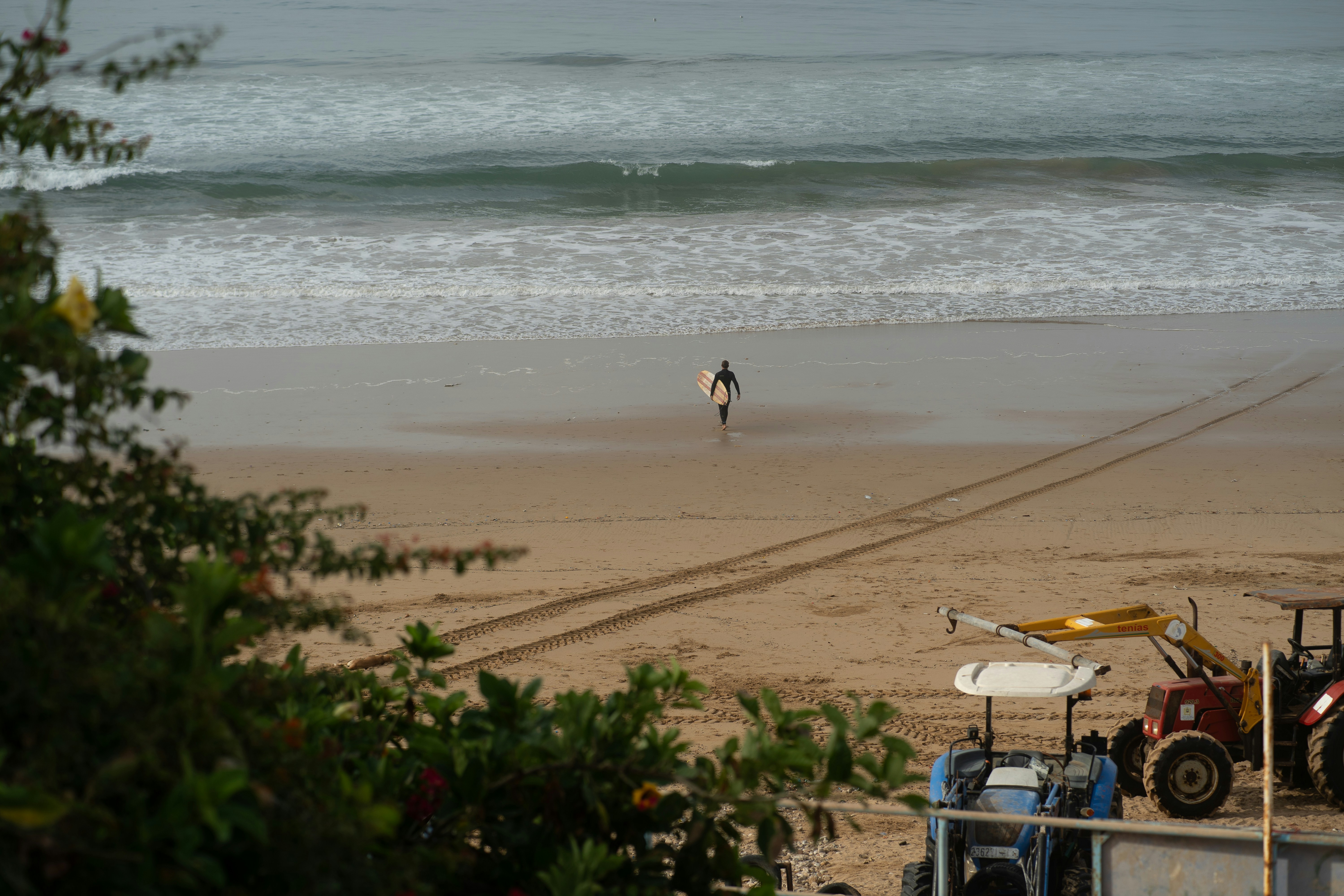 eine Person, die mit einem Surfbrett am Strand spazieren geht