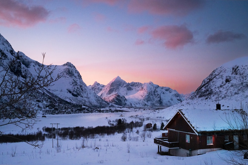 a snowy landscape with a cabin in the foreground and mountains in the background