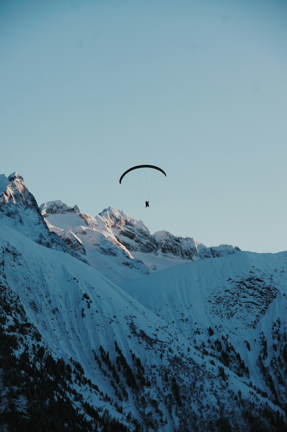 a paraglider is flying over a snowy mountain