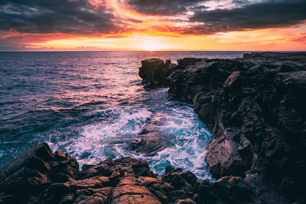 a sunset over the ocean with waves crashing on the rocks