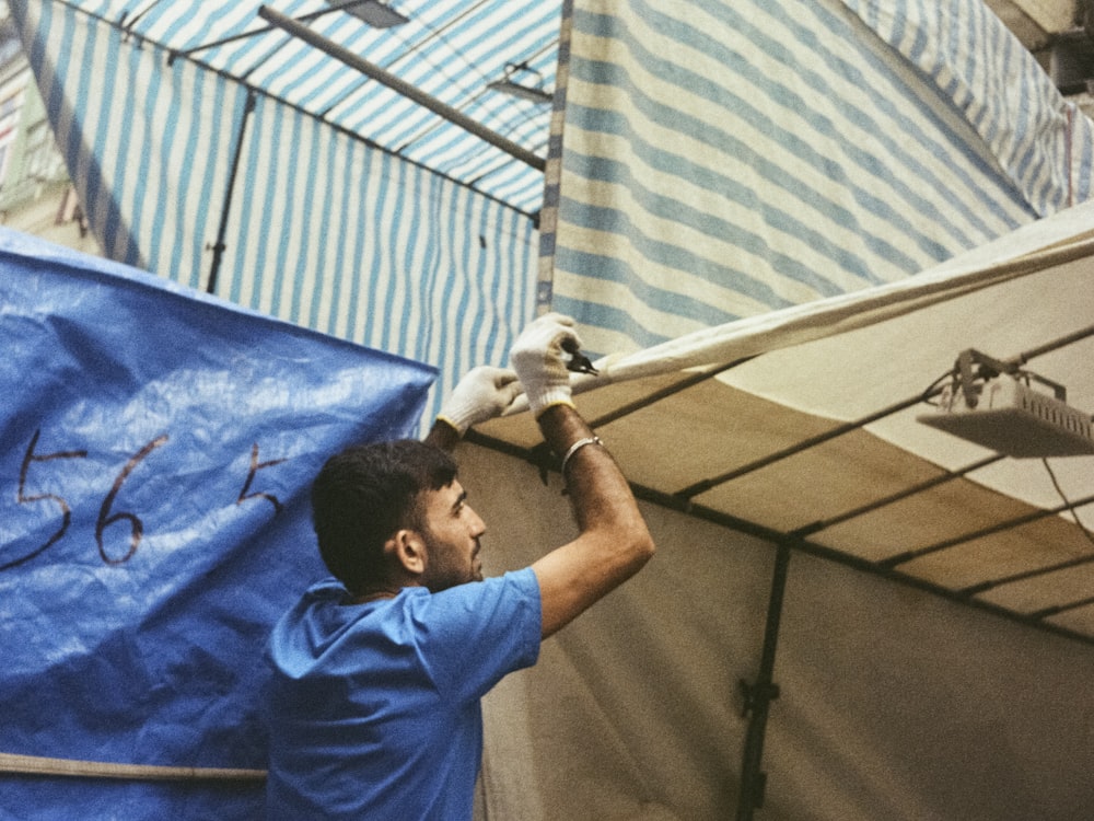 a man in a blue shirt and white gloves working on a tent