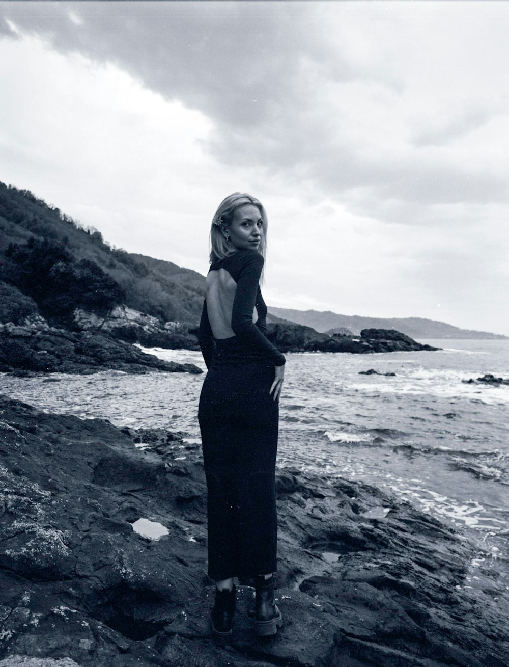 uma mulher em pé em uma praia rochosa ao lado do oceano