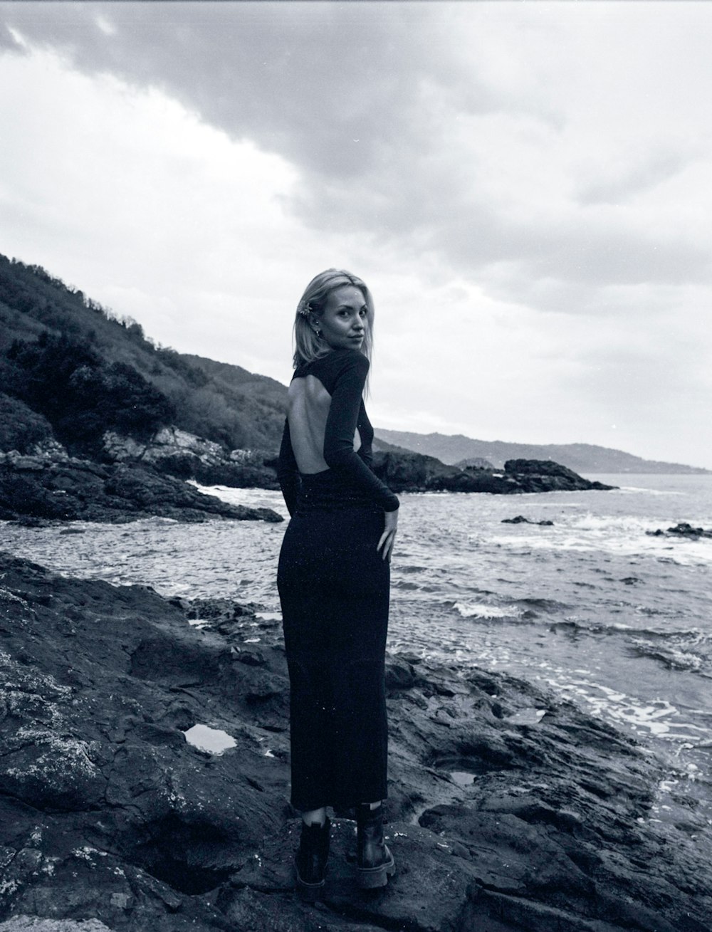 a woman standing on a rocky beach next to the ocean