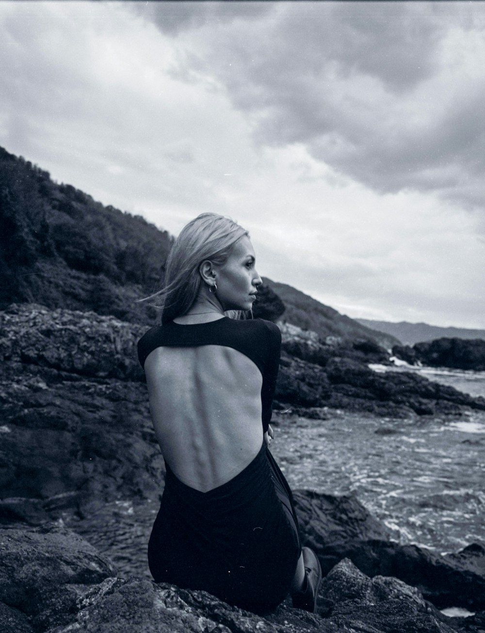 uma mulher sentada em uma rocha perto do oceano