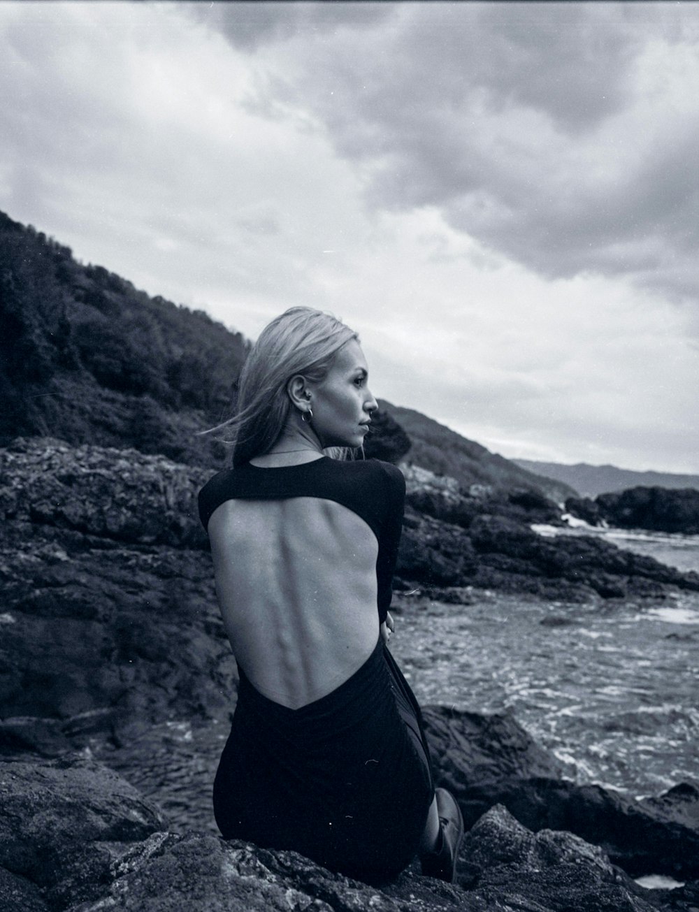 a woman sitting on a rock near the ocean