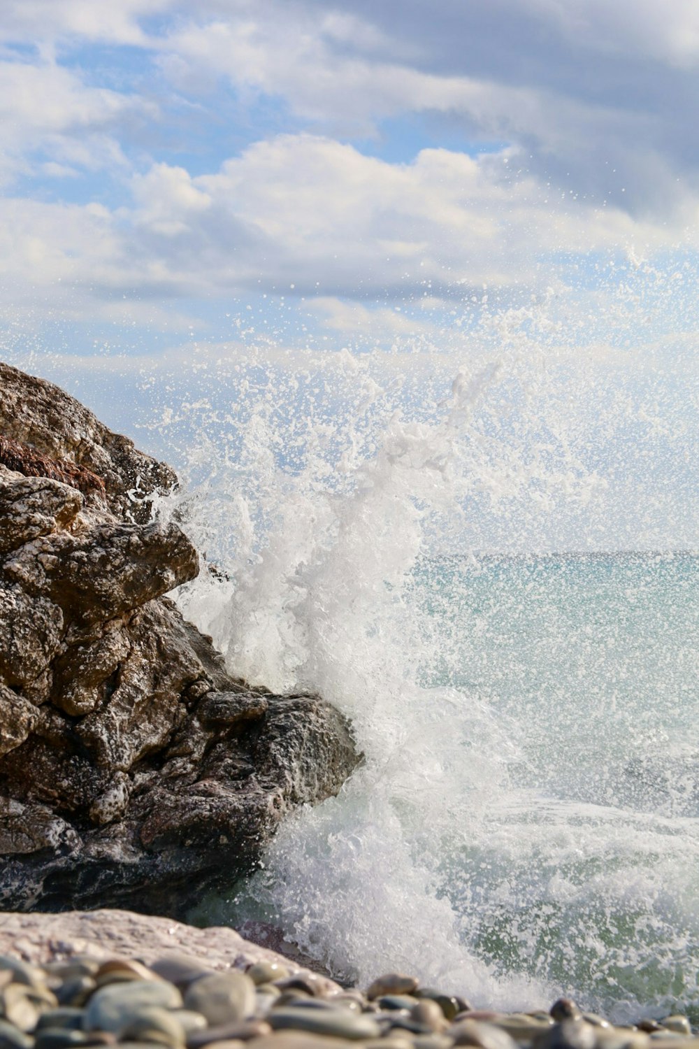 a wave crashes against a rocky shore on a sunny day