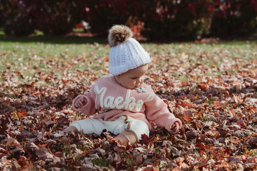 a baby girl sitting in a pile of leaves