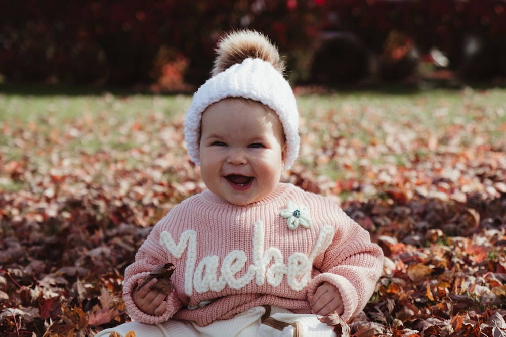 a smiling baby sitting on a pile of leaves