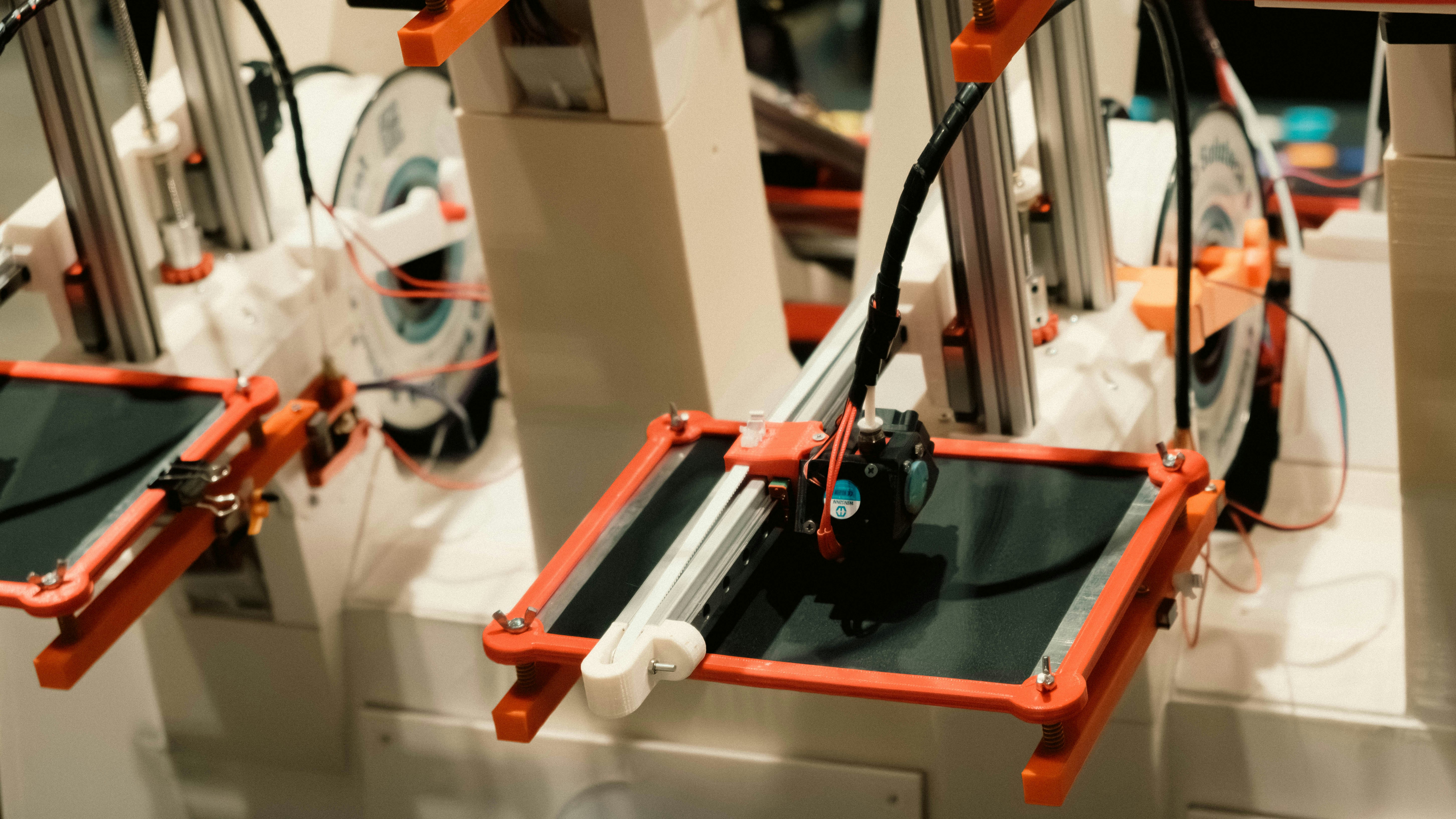 Industrial 3D printing machine producing orange-colored precision components in a clean manufacturing environment