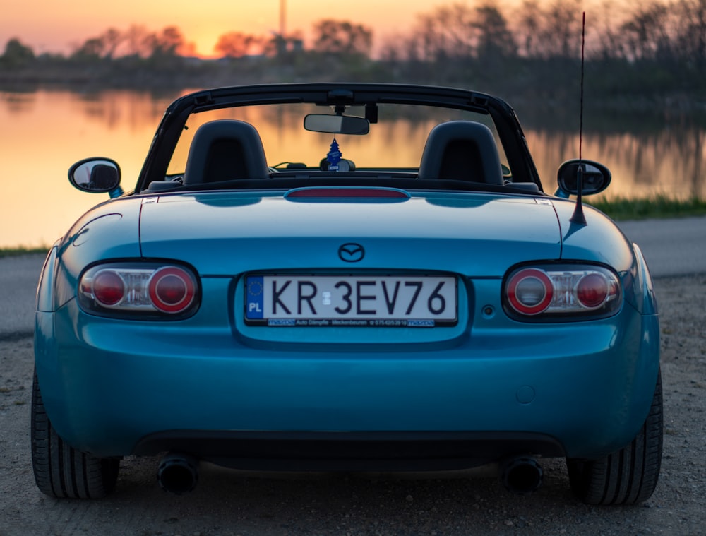 a blue sports car parked in front of a body of water