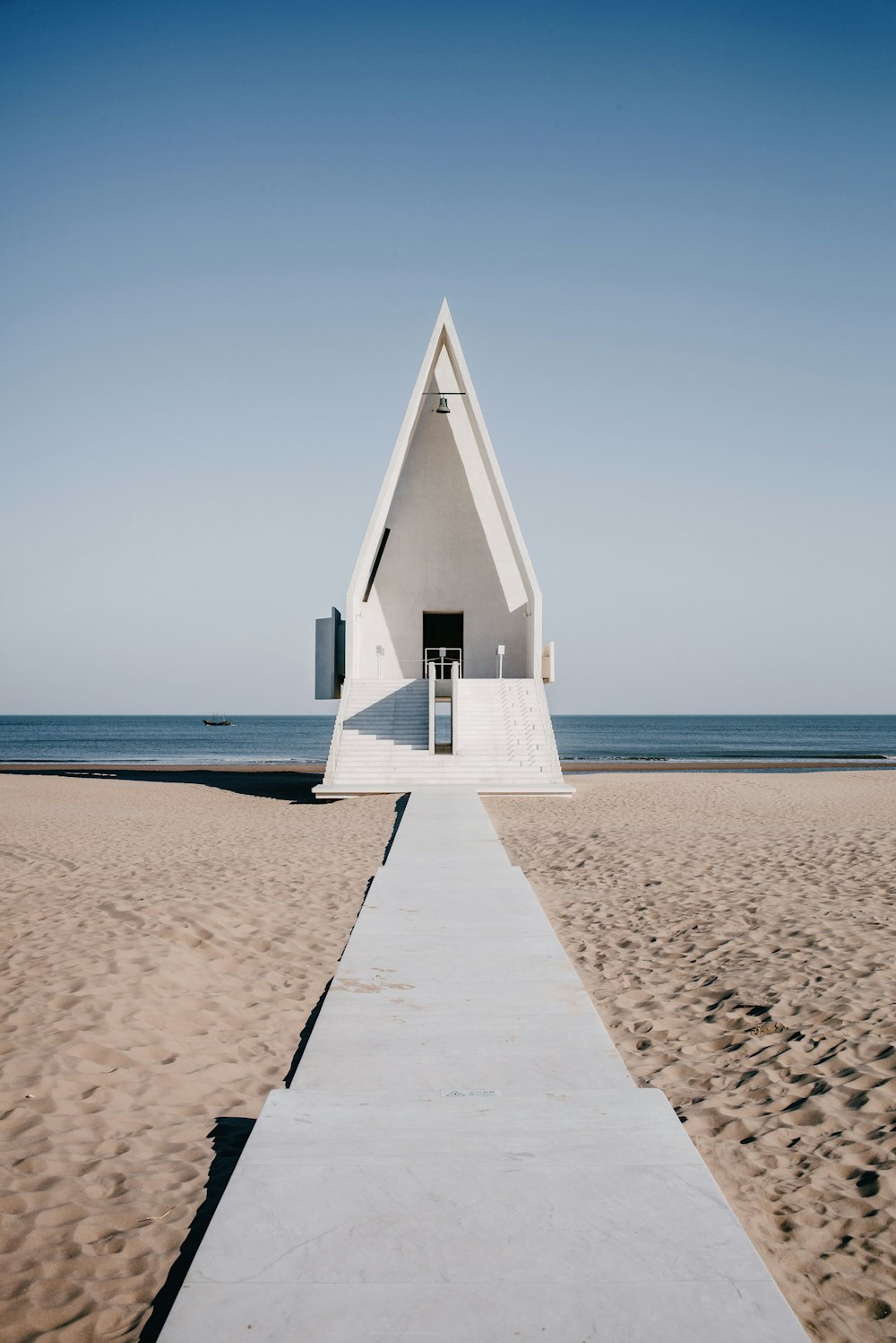 a walkway leading to a white triangular structure on a beach