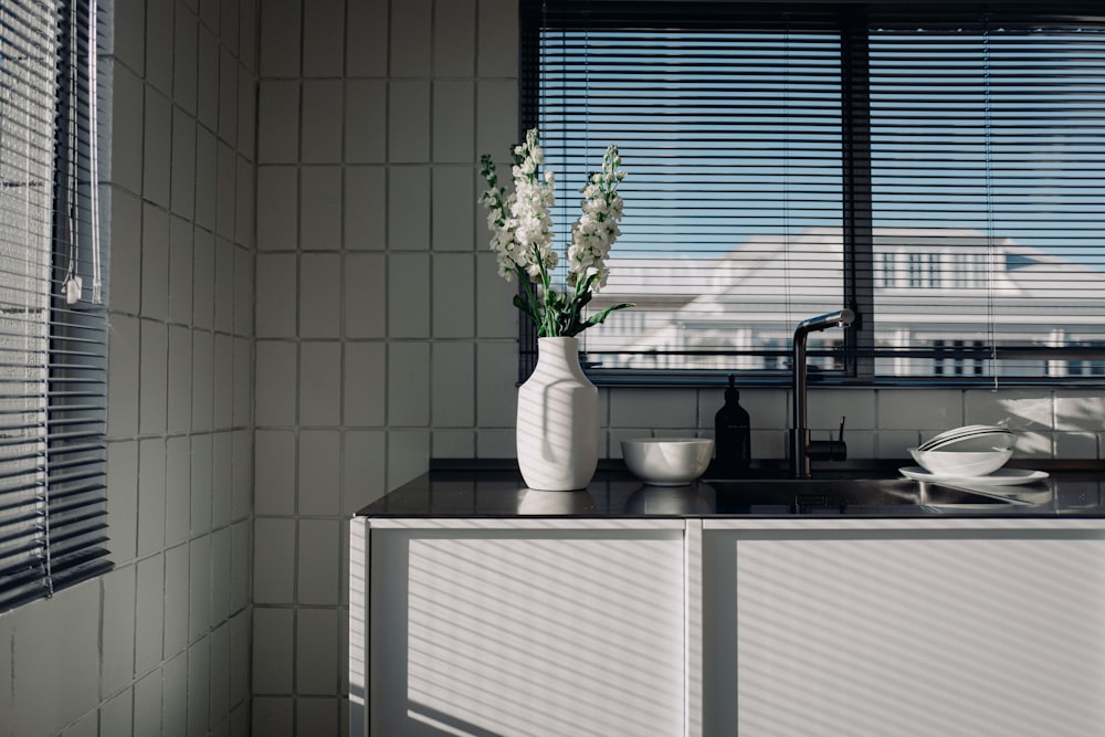 a white vase with flowers on a kitchen counter