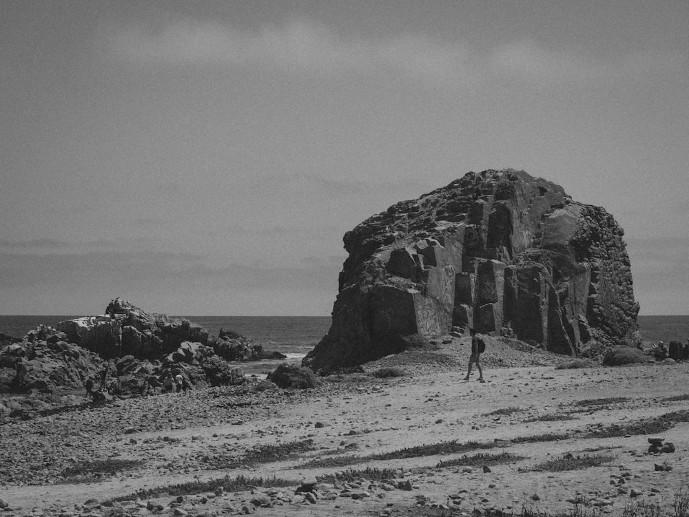 a black and white photo of a person standing in front of a rock formation