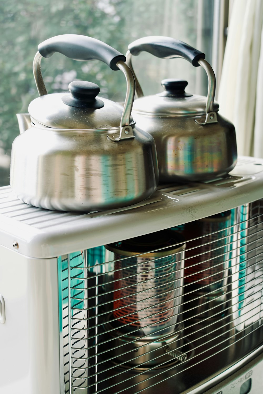 two tea kettles sitting on top of a toaster oven