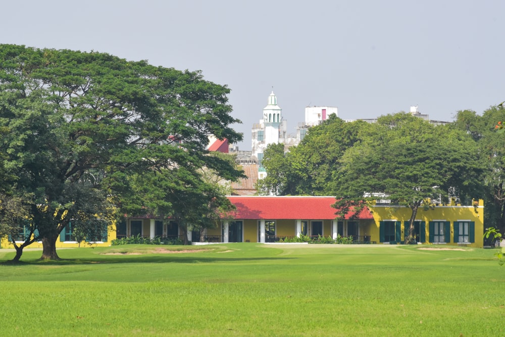 a yellow building with a red roof in the middle of a green field