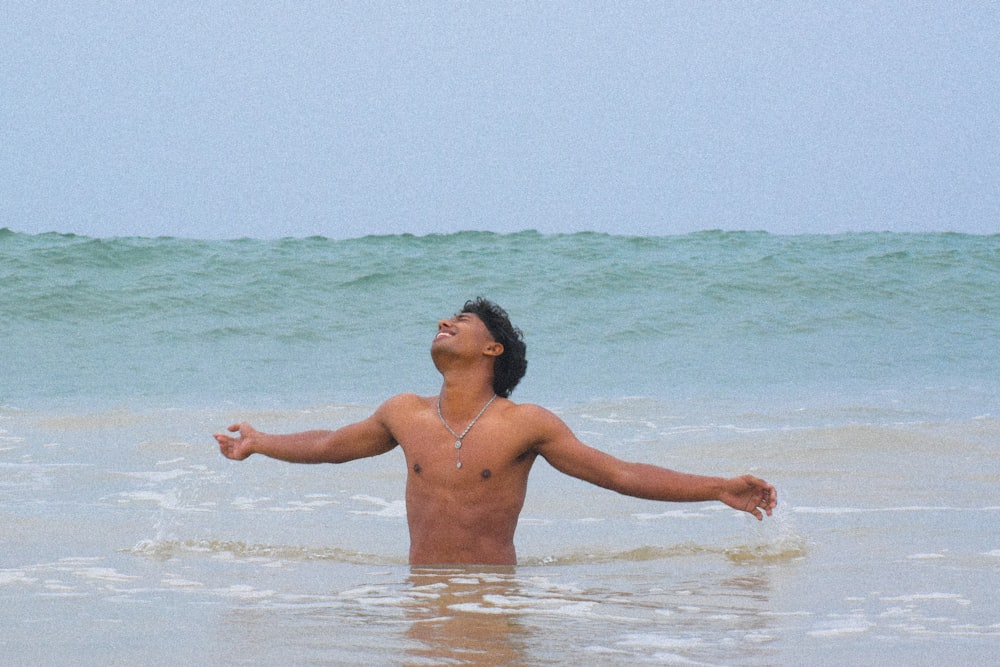 a man standing in the ocean with his arms outstretched