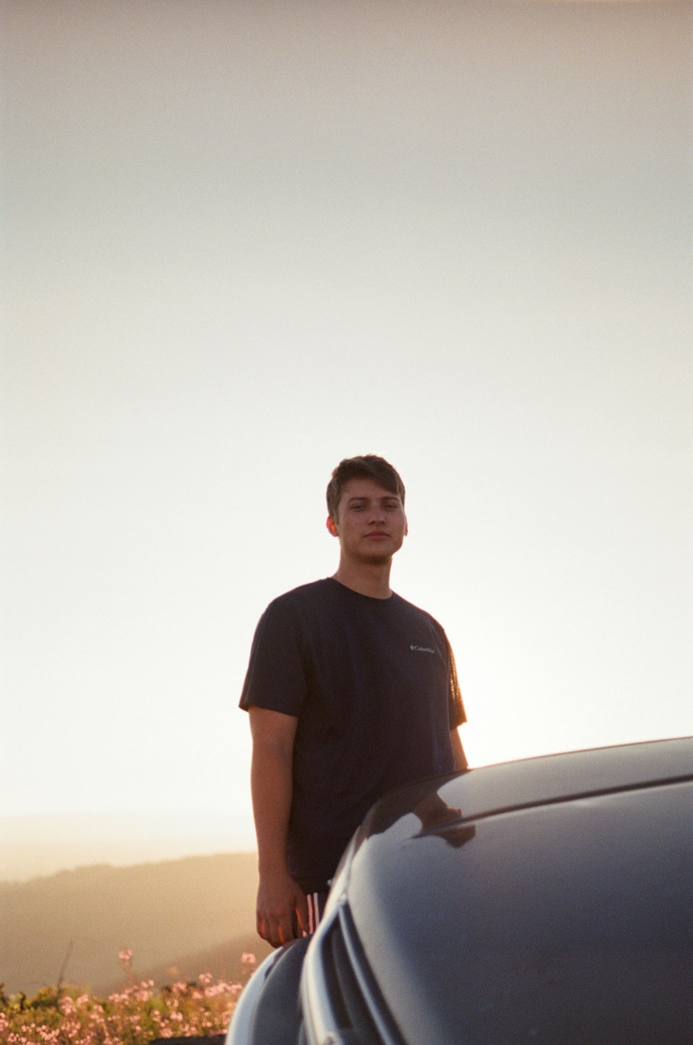 a young man standing next to a parked car