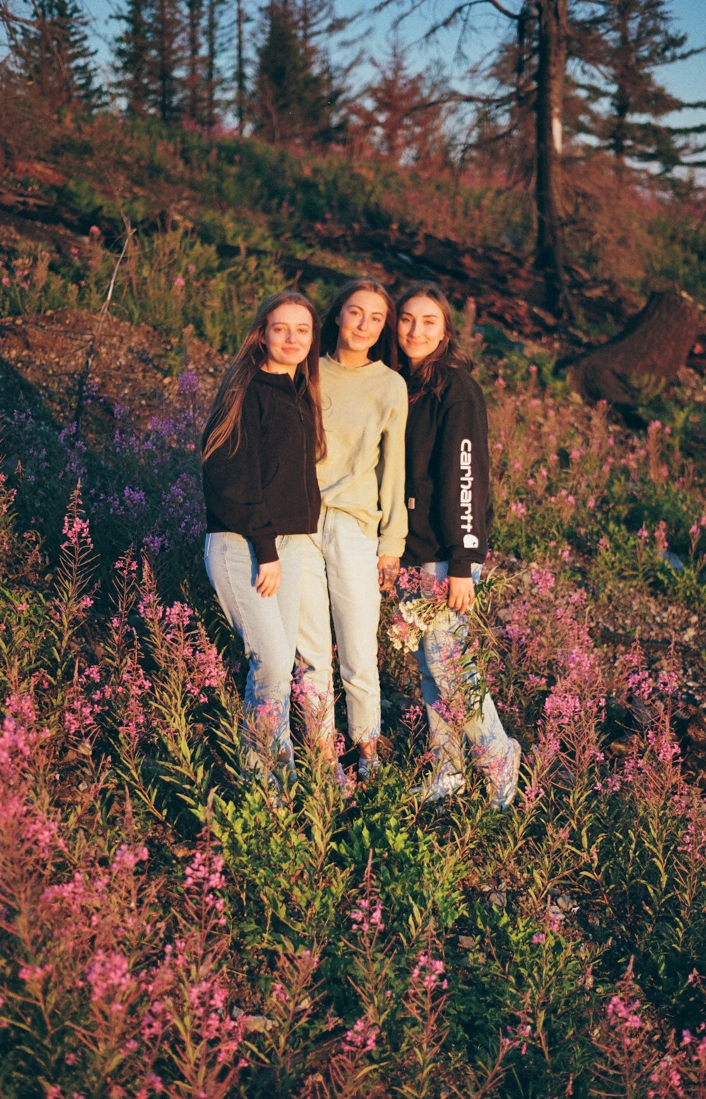 three girls are standing in a field of flowers