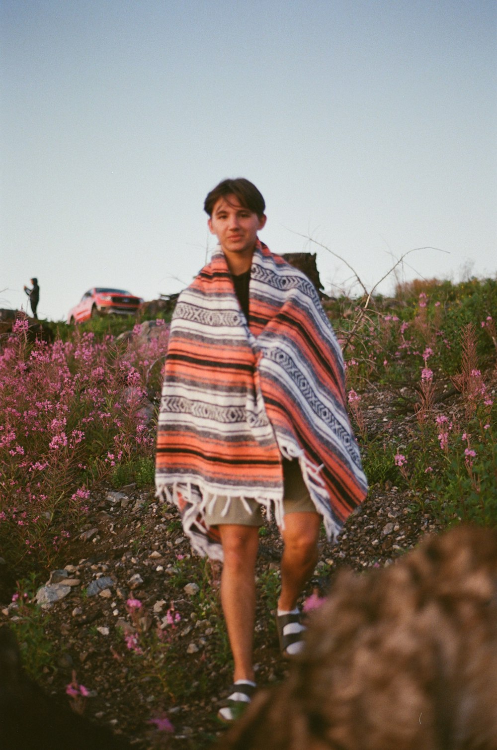 a woman walking down a dirt road carrying a blanket