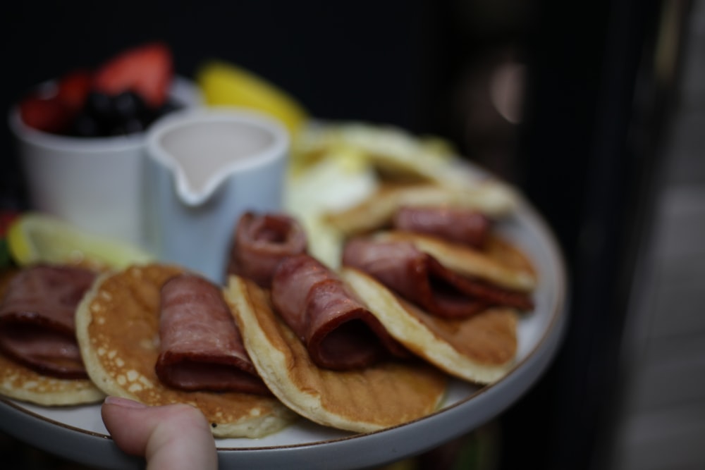 a person holding a plate with pancakes and ham