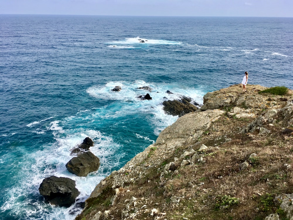 una persona in piedi in cima a una scogliera vicino all'oceano