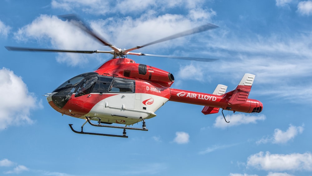 a red and white helicopter flying through a blue sky