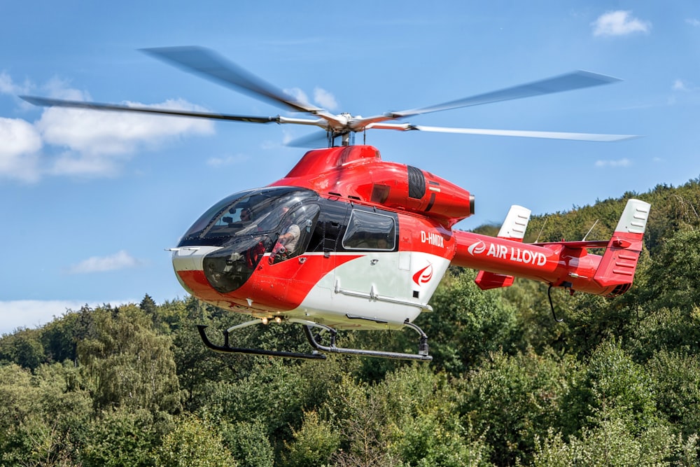 a red and white helicopter flying over a forest