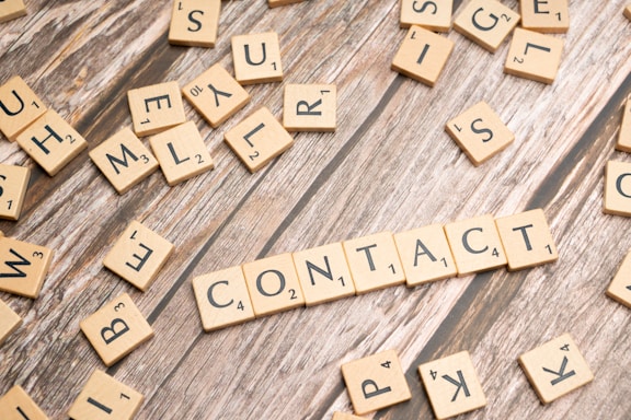 scrabble tiles spelling contact on a wooden surface