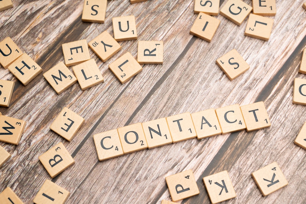 scrabble tiles spelling contact on a wooden surface