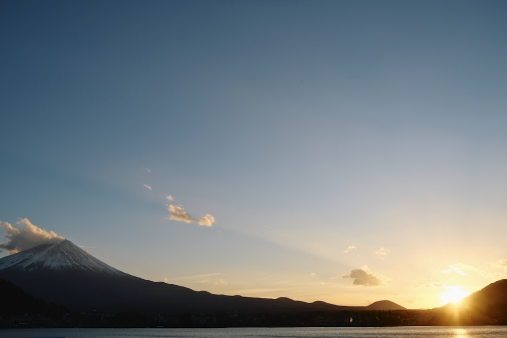 the sun is setting over a mountain and a body of water