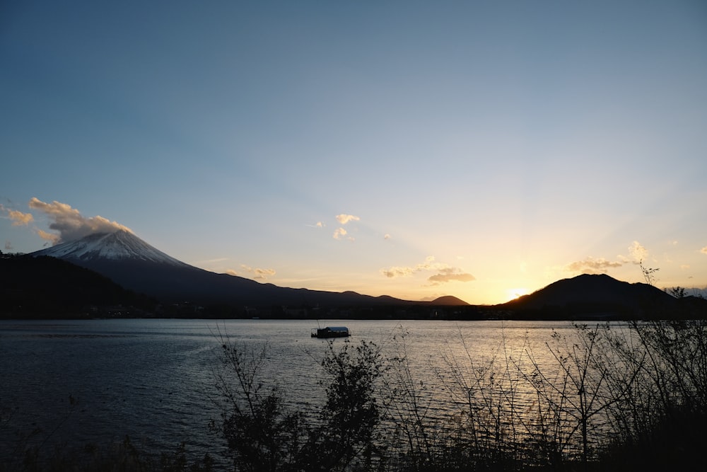 the sun is setting over a lake with a mountain in the background