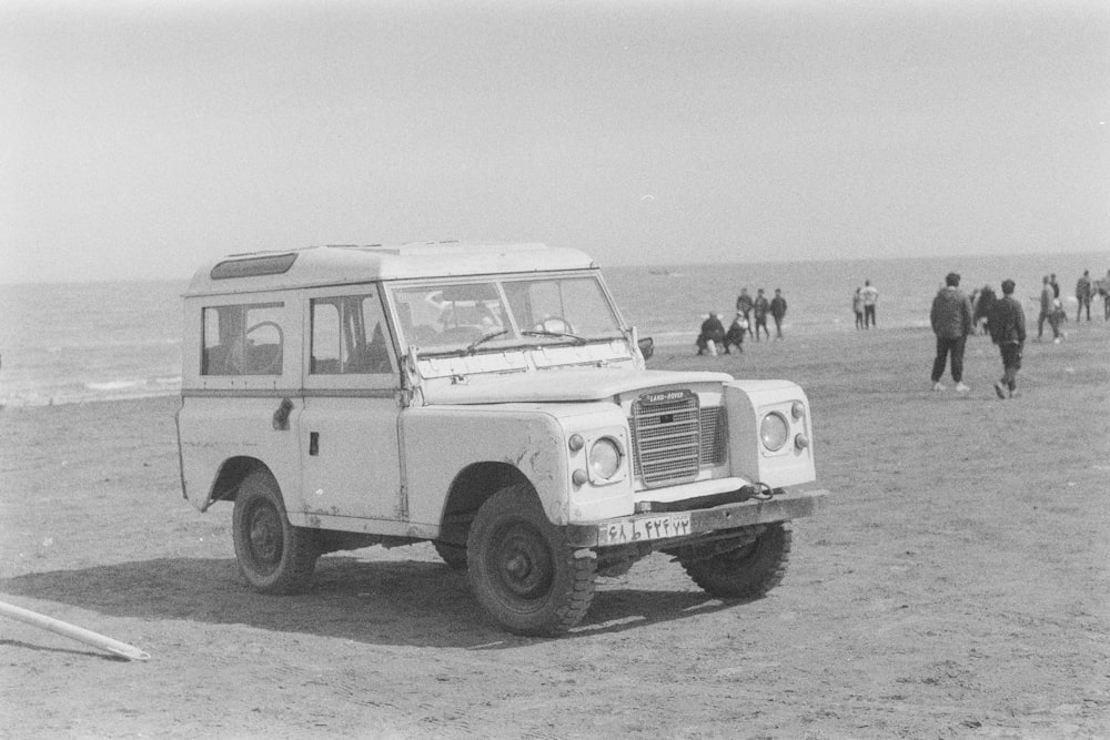 a black and white photo of a land rover on the beach