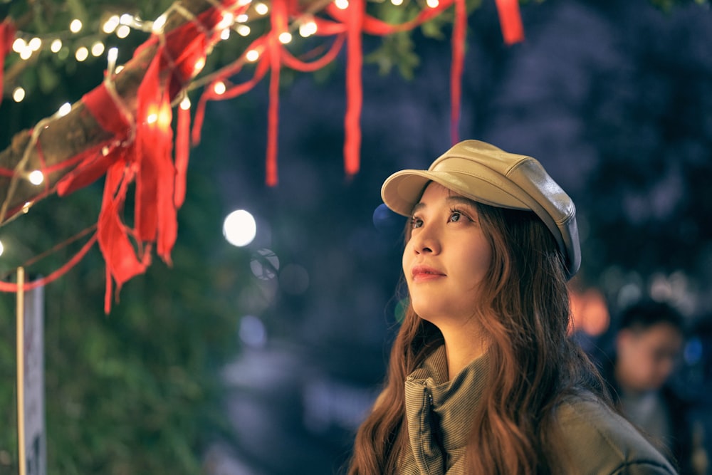 a woman wearing a hat standing under a christmas tree