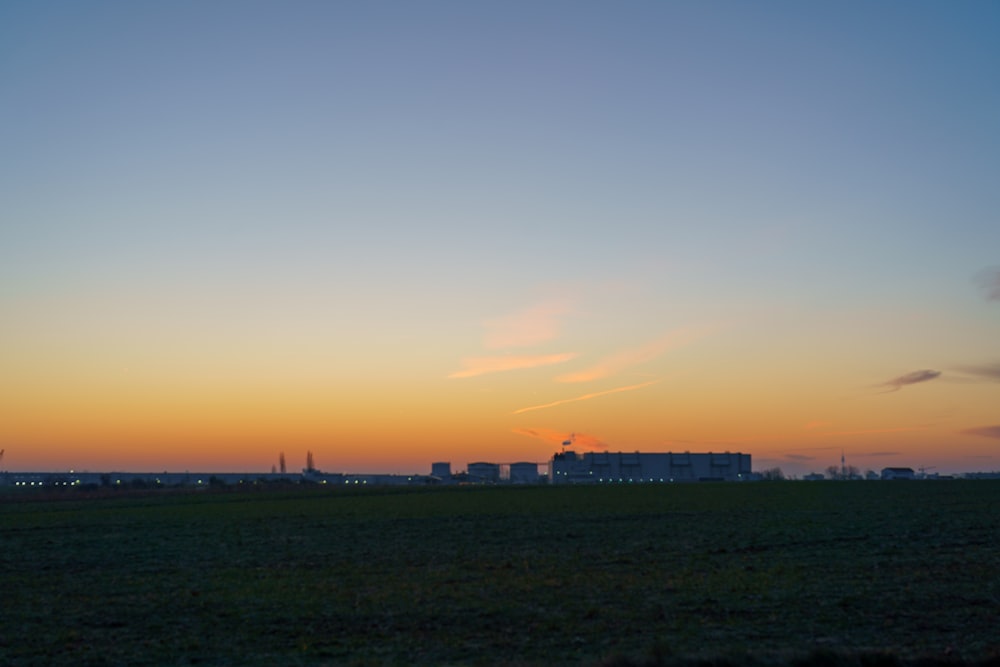 the sun is setting over a field with buildings in the background