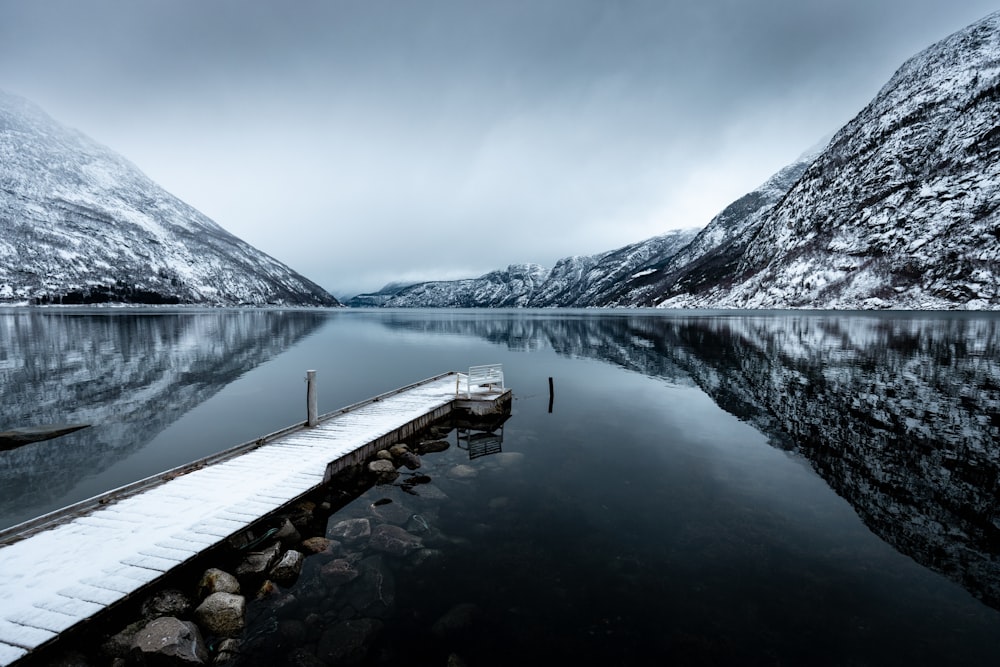 a dock on a lake surrounded by snow covered mountains