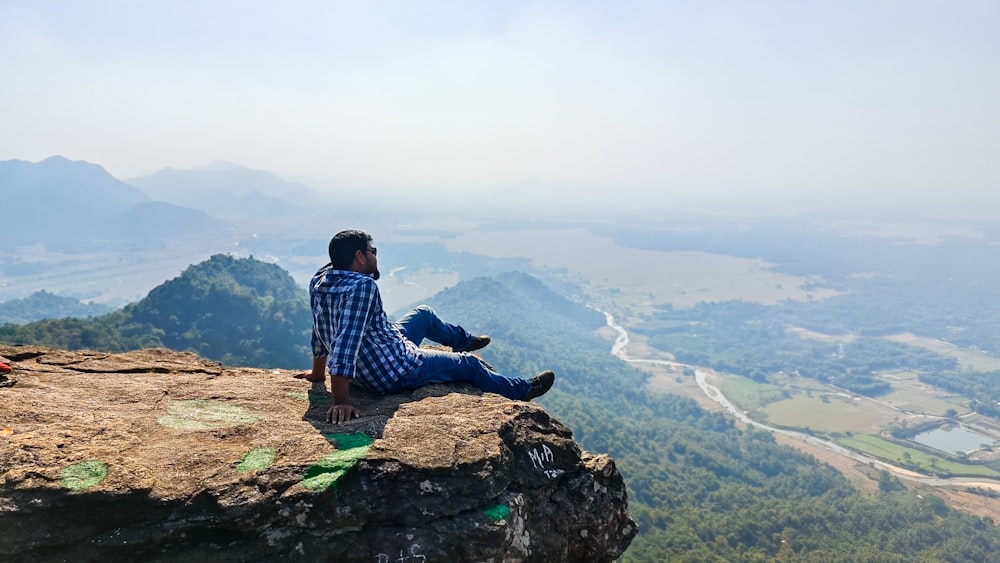 a man sitting on top of a cliff overlooking a valley