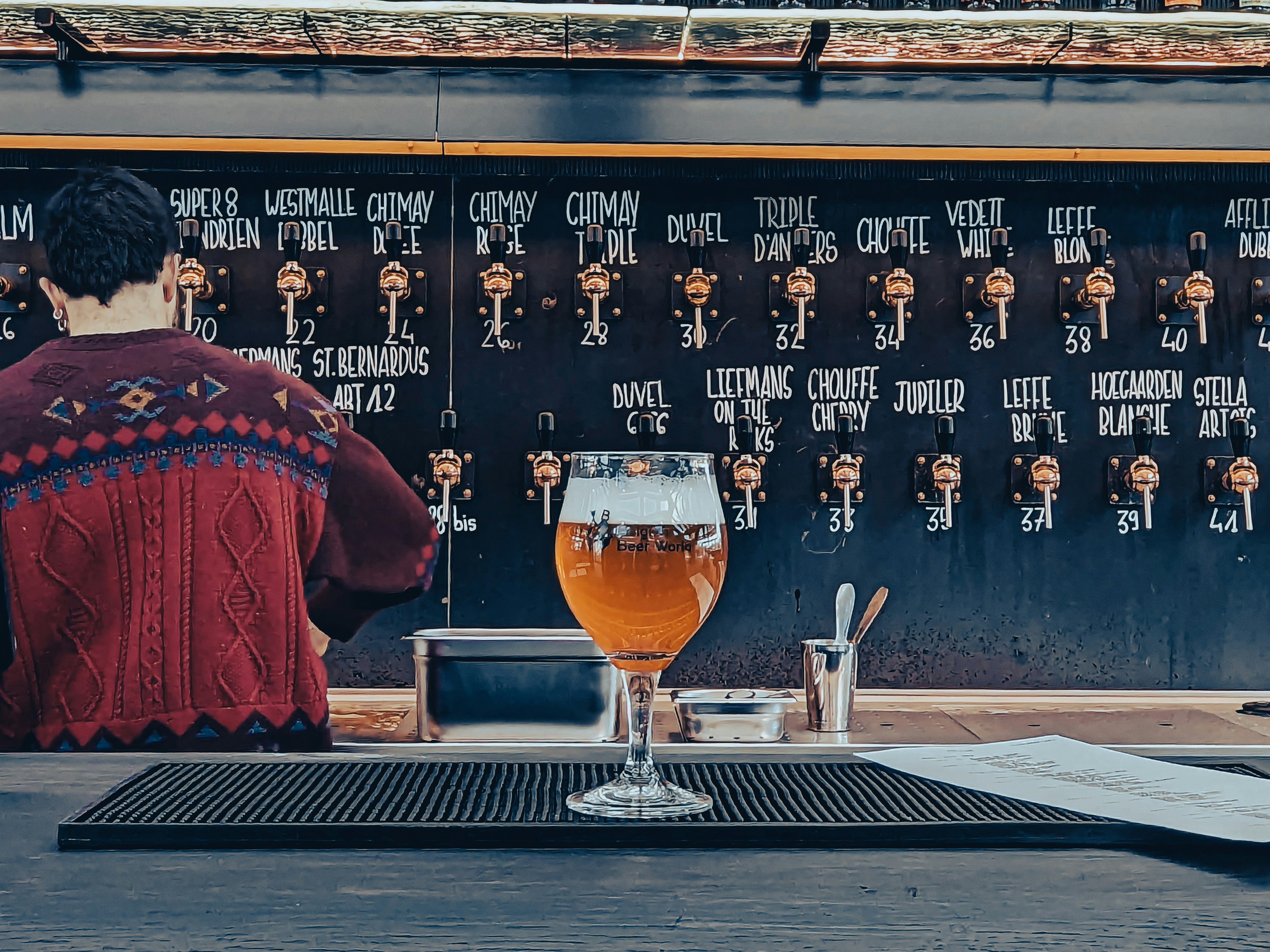 Glass of beer on a bar in front of a tap list wall