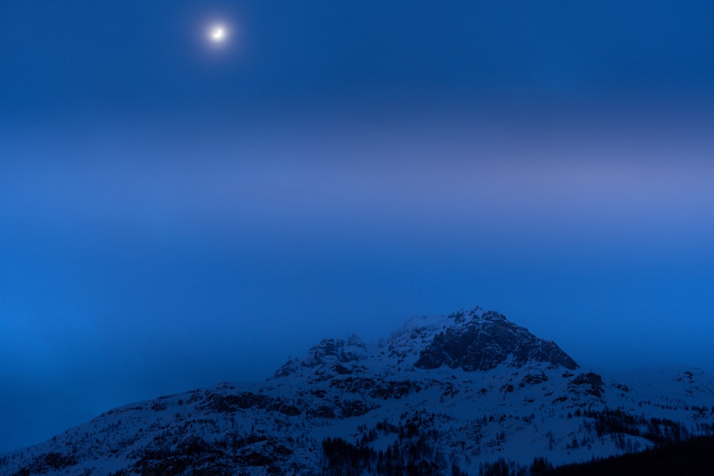 a full moon is seen above a snowy mountain