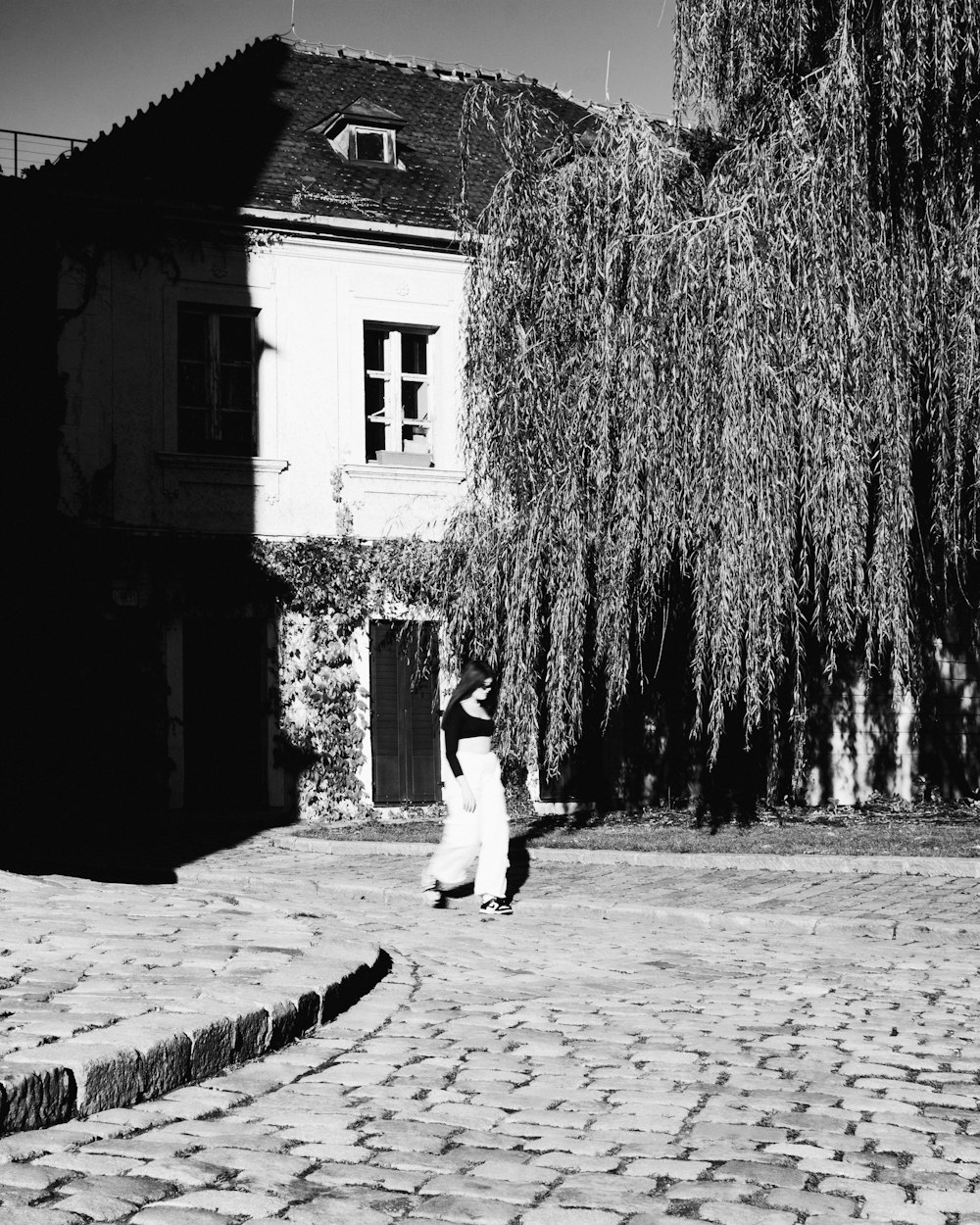 a woman walking down a cobblestone street next to a tree