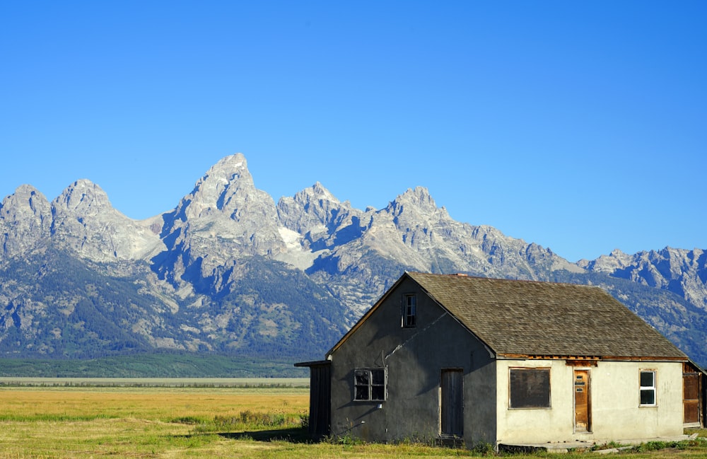 an old house in a field with mountains in the background