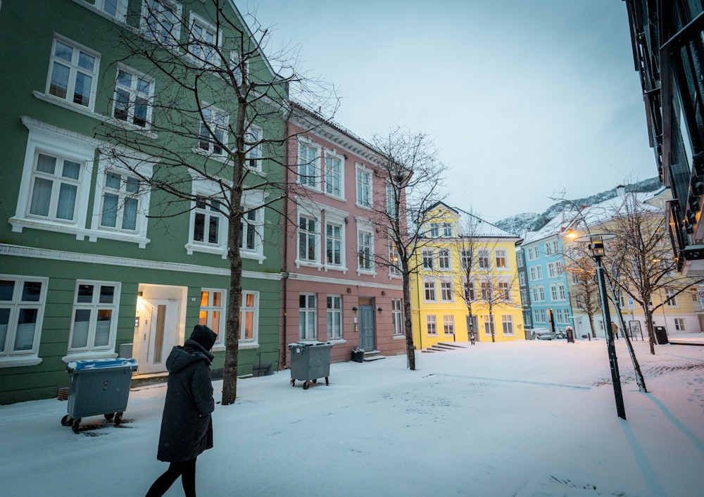 a person walking in the snow in front of a row of buildings
