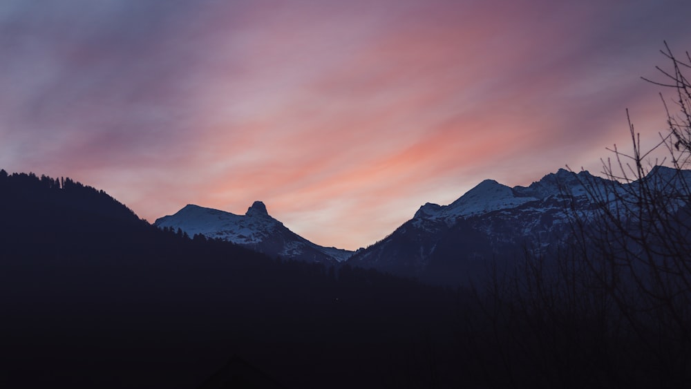 a sunset view of a mountain range with trees in the foreground