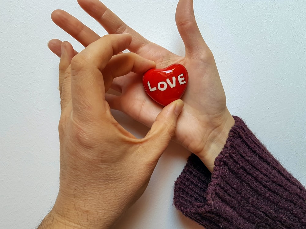 two hands holding a red heart with the word love written on it