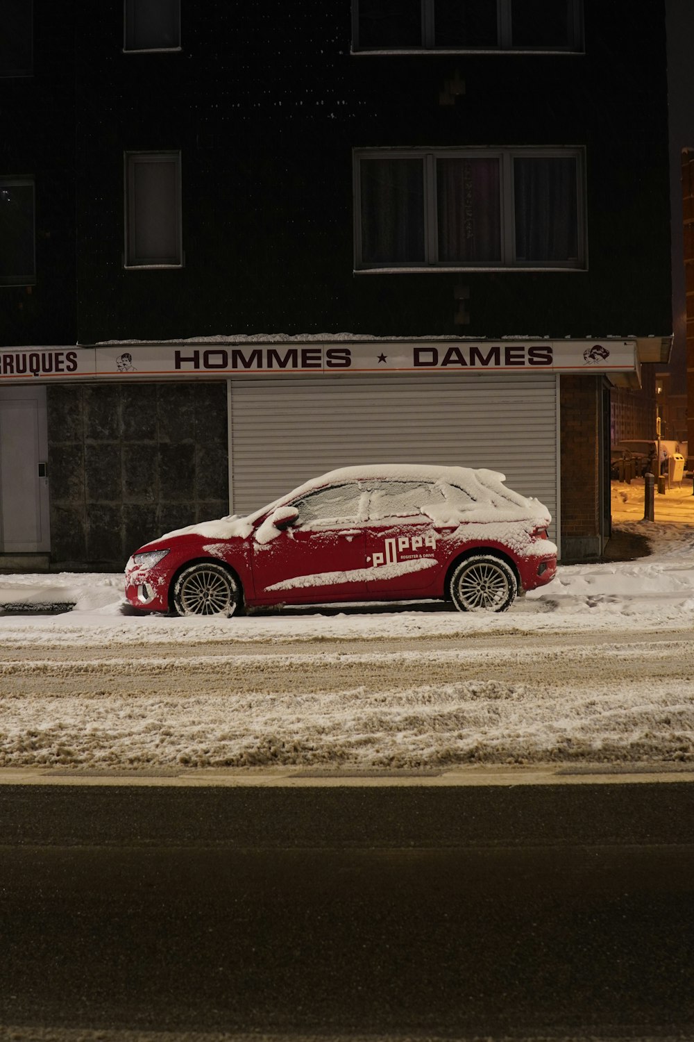 a red car parked in front of a building covered in snow