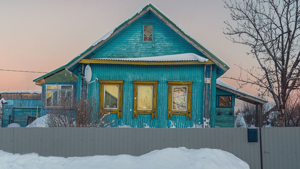 a blue house with yellow windows and snow on the ground