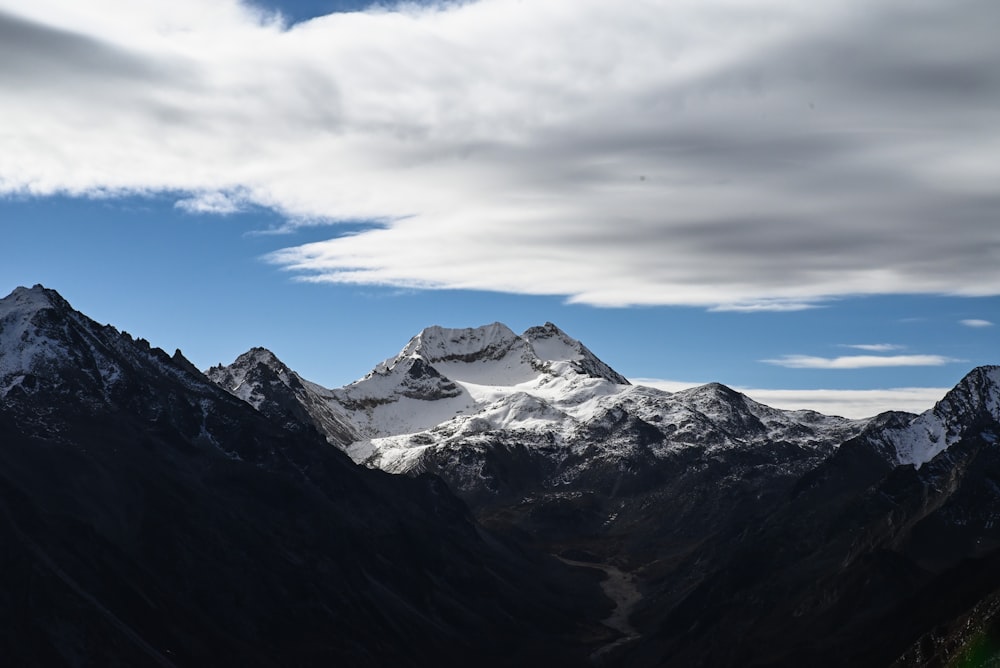 a snow covered mountain range under a cloudy blue sky