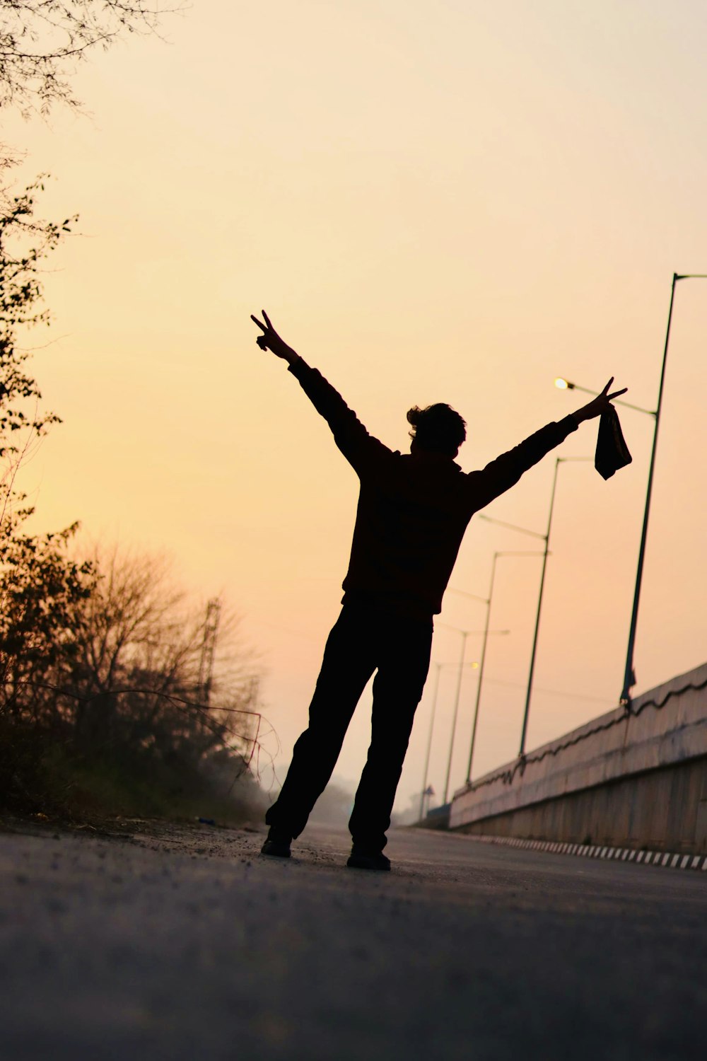 a man standing on the side of a road holding his arms up