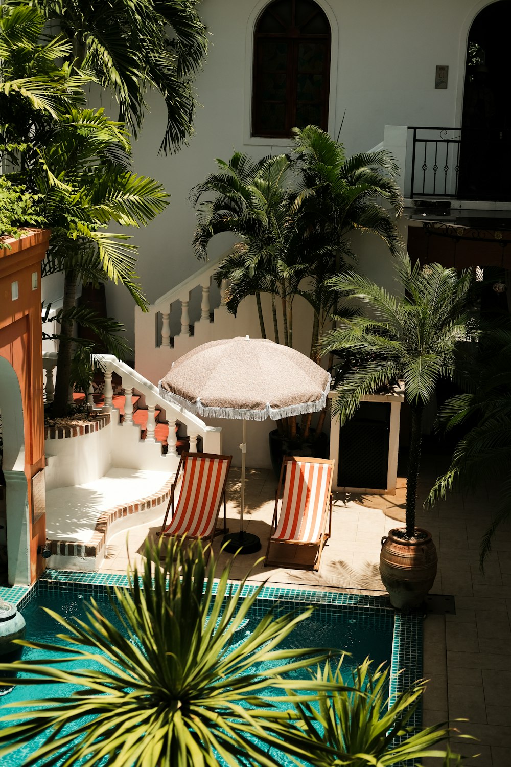 a patio with an umbrella and chairs next to a pool