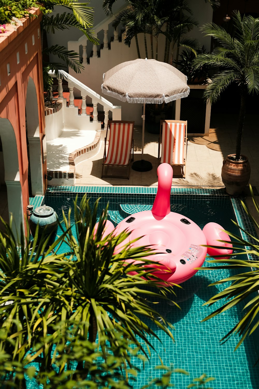 an inflatable pink flamingo sitting in a pool next to a palm tree