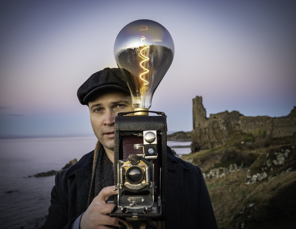 a man holding a camera with a light bulb on top of it